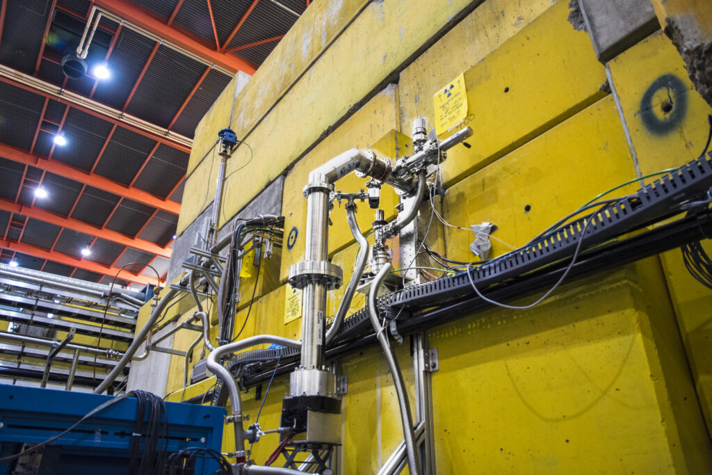 A series of reflective metal tubes exiting a large wall of yellow concrete blocks.