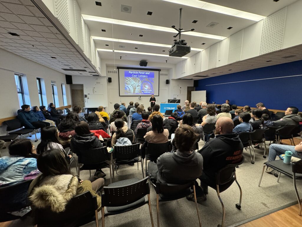 A large audience of people seated facing a lecturer and a screen