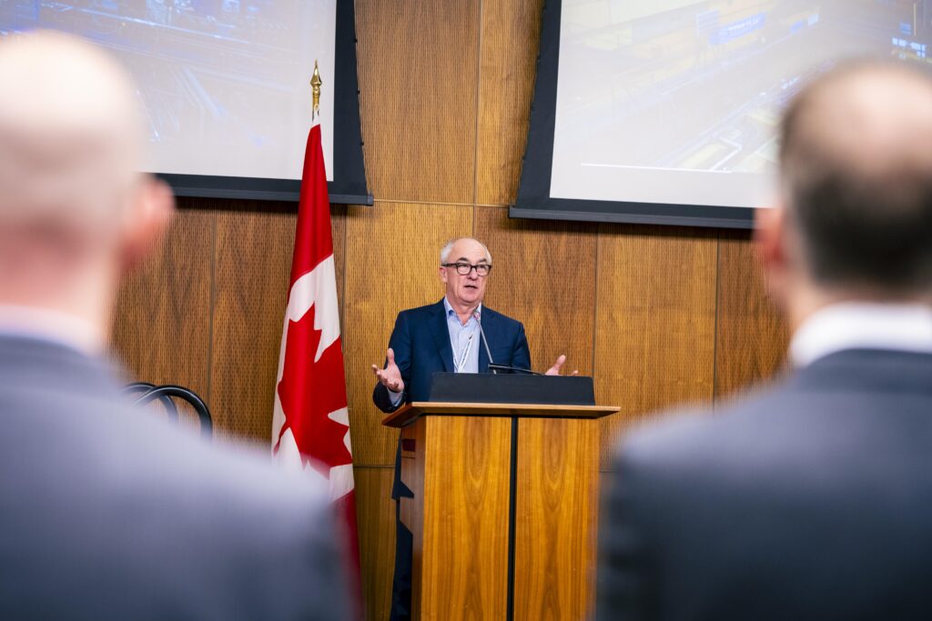 A man stands in front of a podium, speaking to an audience.