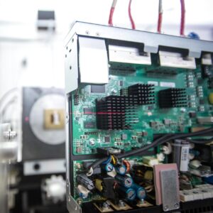 A green computer board stands upright on a table, with a red laser crosshatch pointed at a specific black component